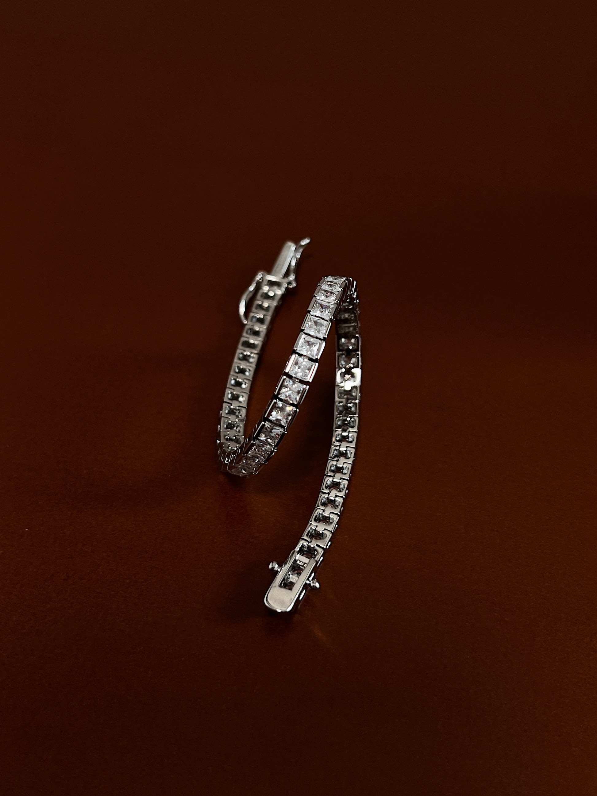 Coiled view displaying the fluid articulated link structure and edge-to-edge metallic channel holding 3mm square-cut cubic zirconia stones on a deep brown surface.