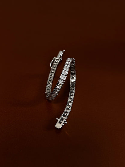 Coiled view displaying the fluid articulated link structure and edge-to-edge metallic channel holding 3mm square-cut cubic zirconia stones on a deep brown surface.