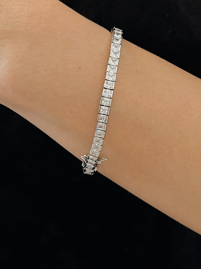 Side angle view of a silver square tennis bracelet styled on a wrist with a black tailored top, showing the secure box clasp and fluid drape for elegant jewellery layering.