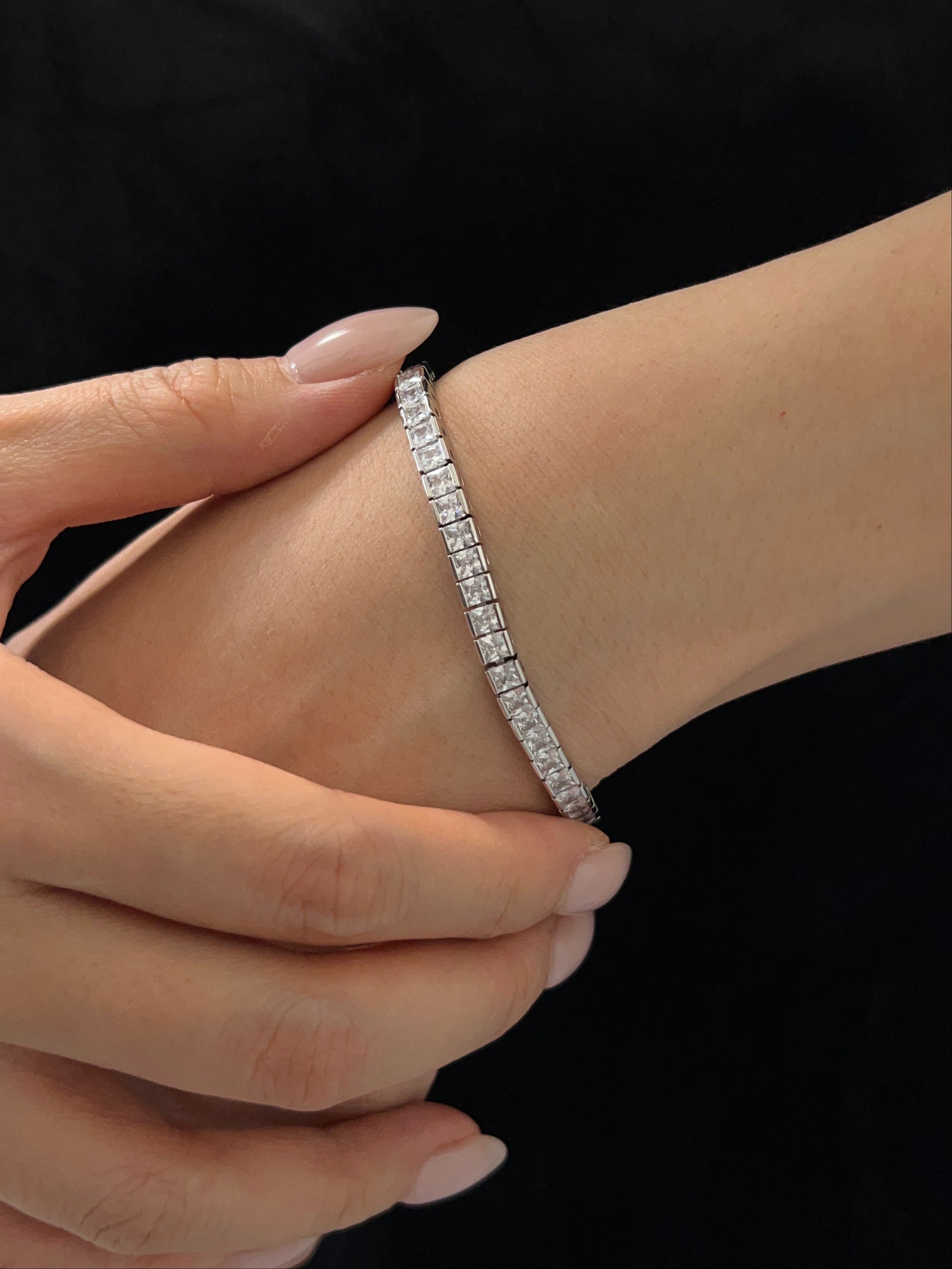 Close-up view of a silver channel set tennis bracelet with square princess-cut cubic zirconia worn on a wrist against a black outfit