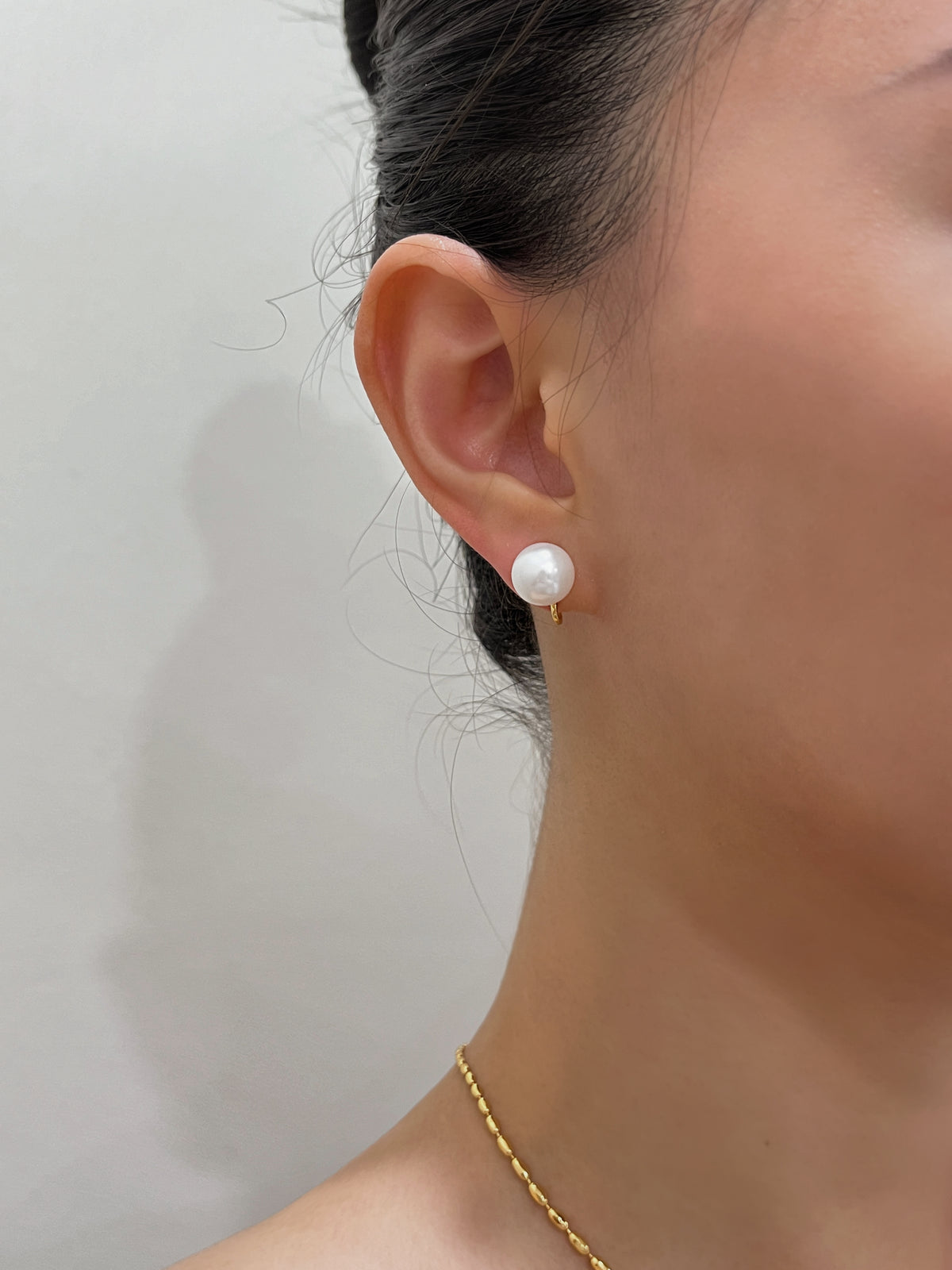 Side profile shot of model wearing a floating 10mm pearl clip-on stud against radiant skin.