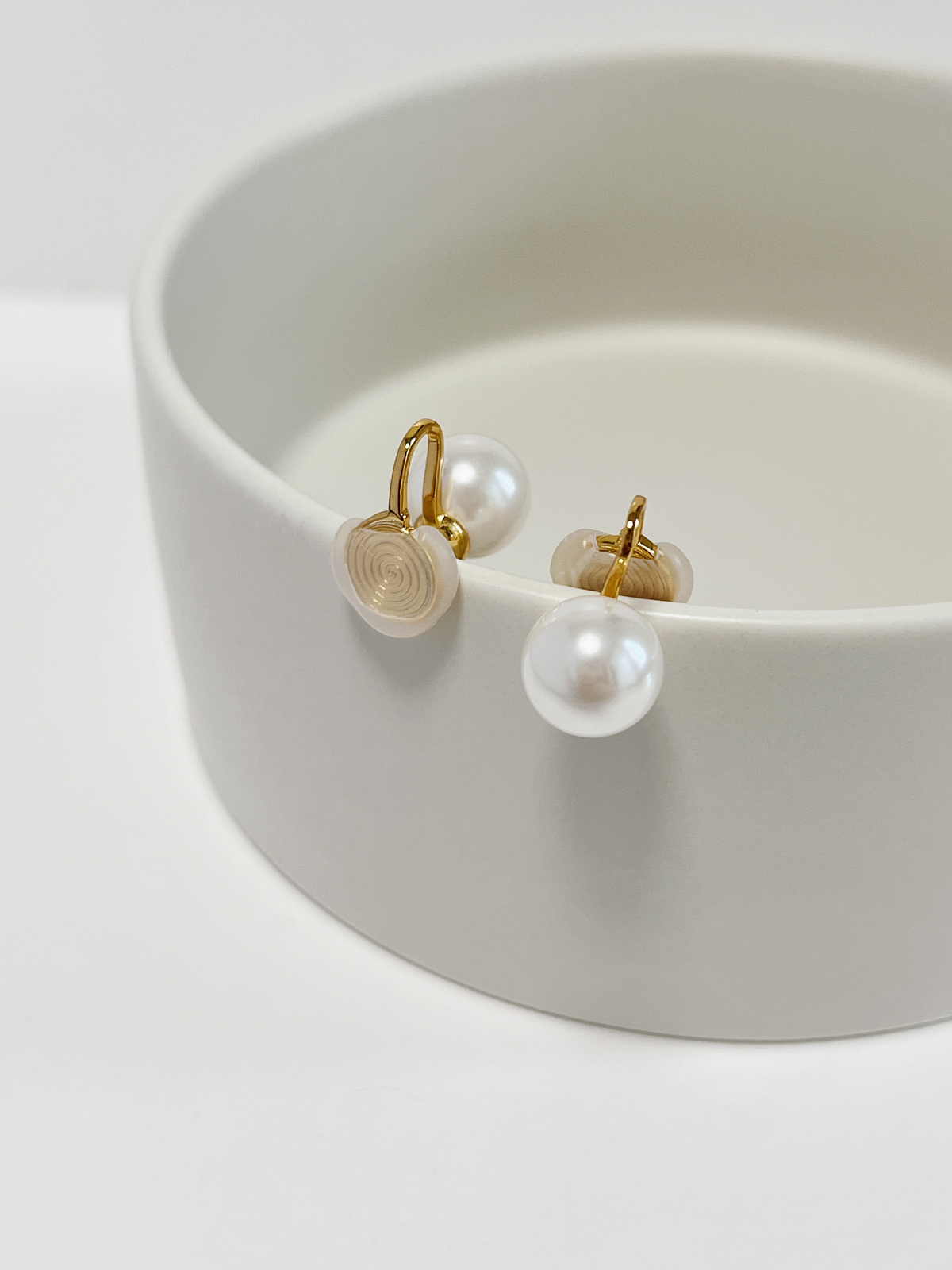 Structural side view of 10mm pearl clip-on studs balancing on a tray rim, demonstrating the flexible U-shaped wire clip and backing depth.