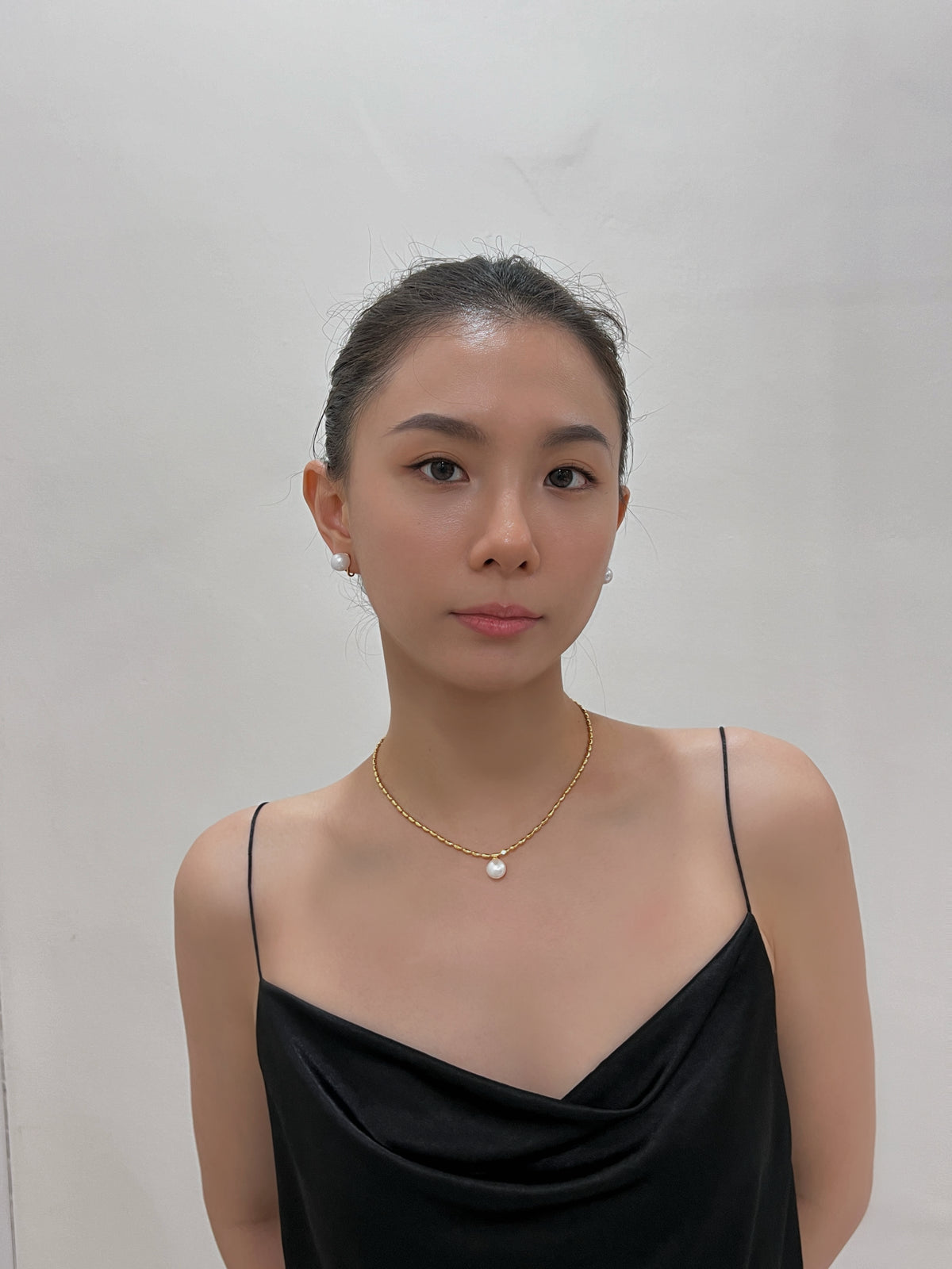 Model styled in a black satin camisole wearing 10mm non-pierced pearl clip-on studs and a matching gold pearl necklace.