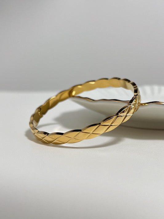 The textured Corin quilted bangle in a polished 18k gold finish, resting elegantly on a minimalist white ceramic plate.