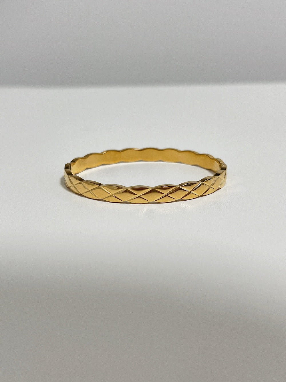 A clean studio product shot of the Corin gold quilted hinged bangle resting flat on a white surface, demonstrating its continuous geometric lattice pattern.