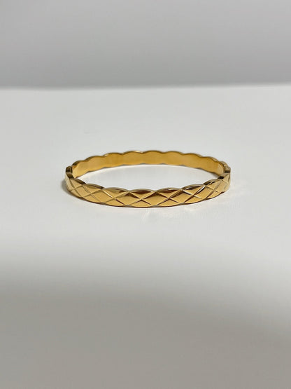 A clean studio product shot of the Corin gold quilted hinged bangle resting flat on a white surface, demonstrating its continuous geometric lattice pattern.