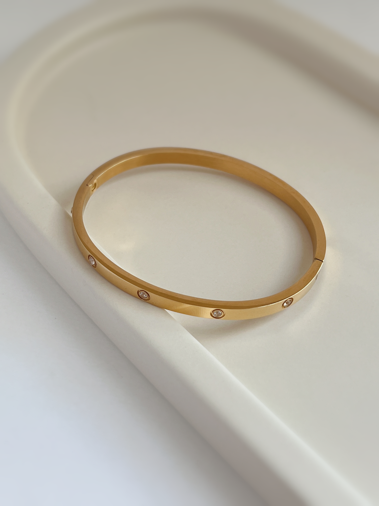 A close-up of the Dane gold six-stone gemstone bangle resting on a minimal white ceramic tray, showcasing the bezel-set crystals.