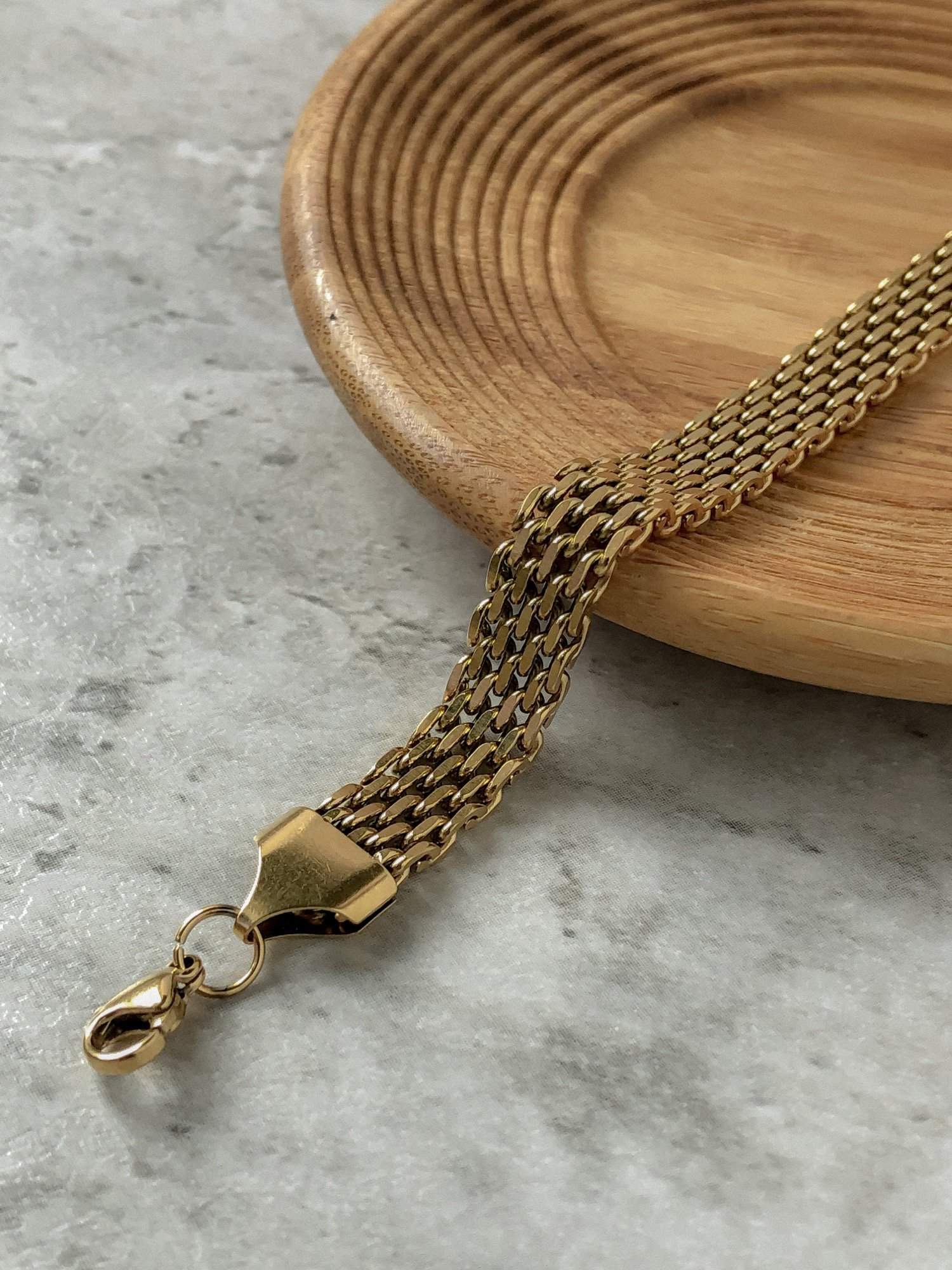 The Danielle gold mesh chain bracelet elegantly cascading over a minimalist circular wooden dish, emphasizing its fluid textile-like texture.