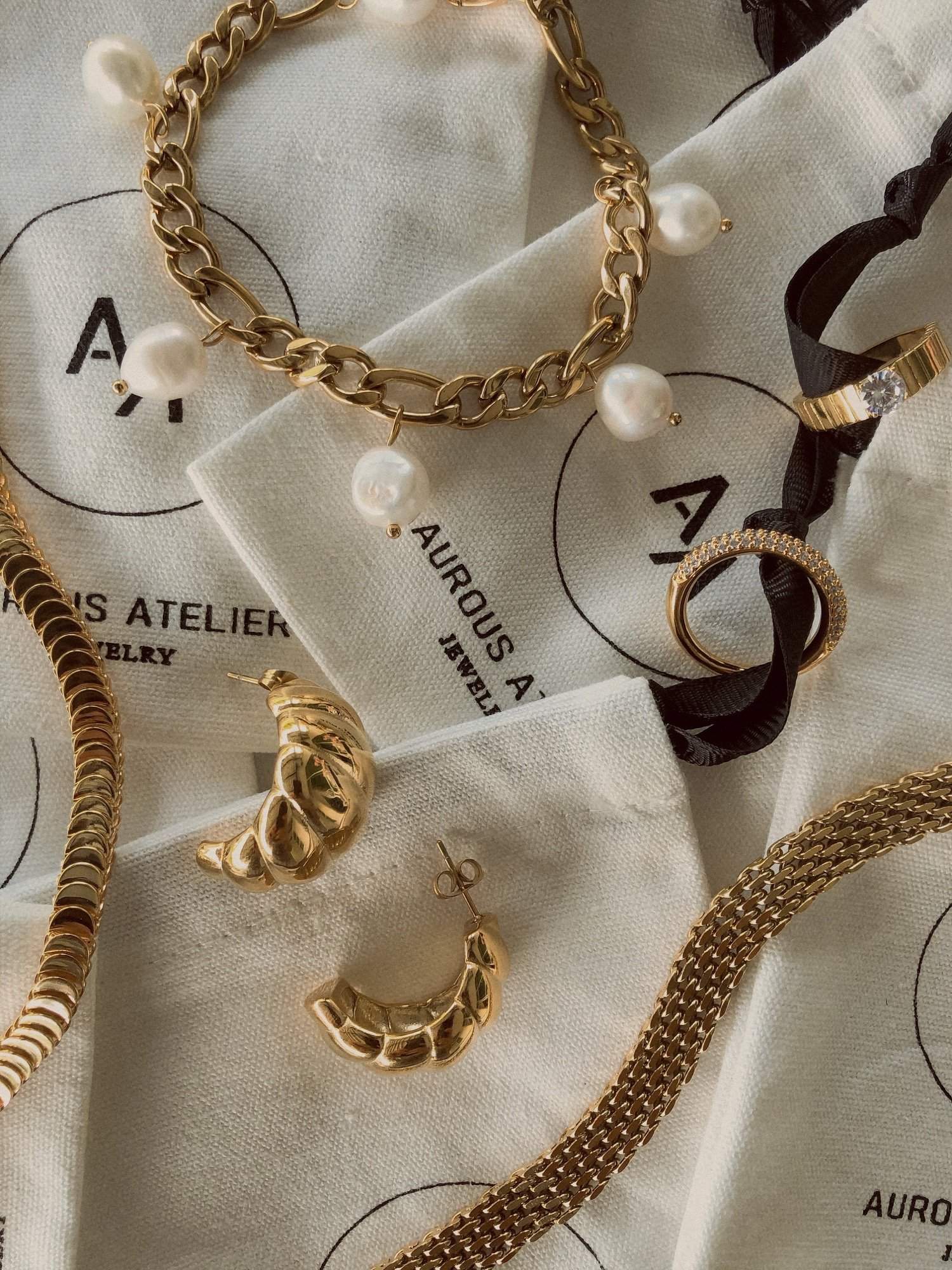 A high-end flat lay showcasing the gold Danielle mesh chain bracelet alongside textured jewelry pouches, fine rings, and pearl links at Aurous Atelier.