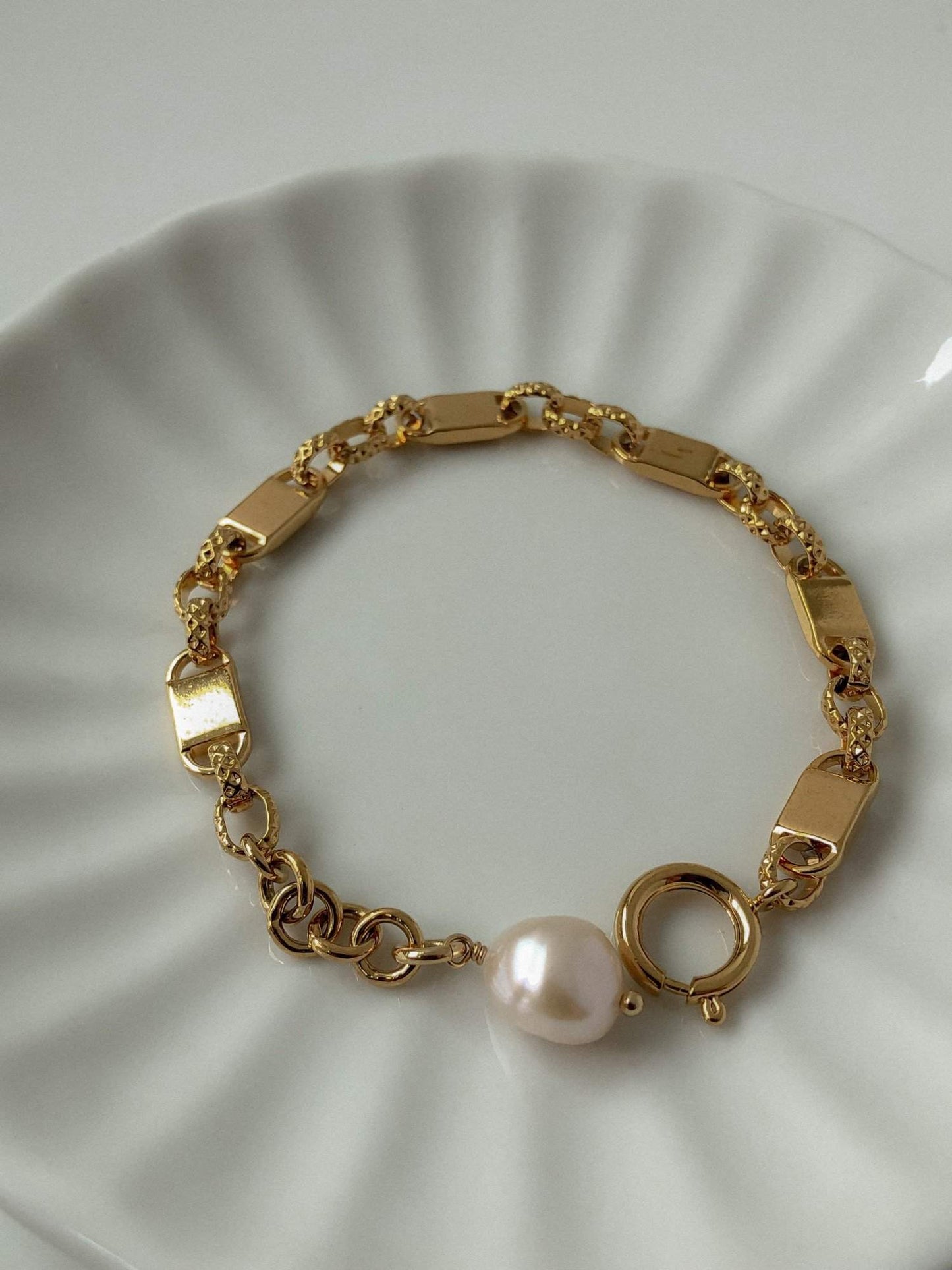A premium top-down product shot of the Diana gold pearl chain bracelet coiled inside a white fluted porcelain jewelry dish.