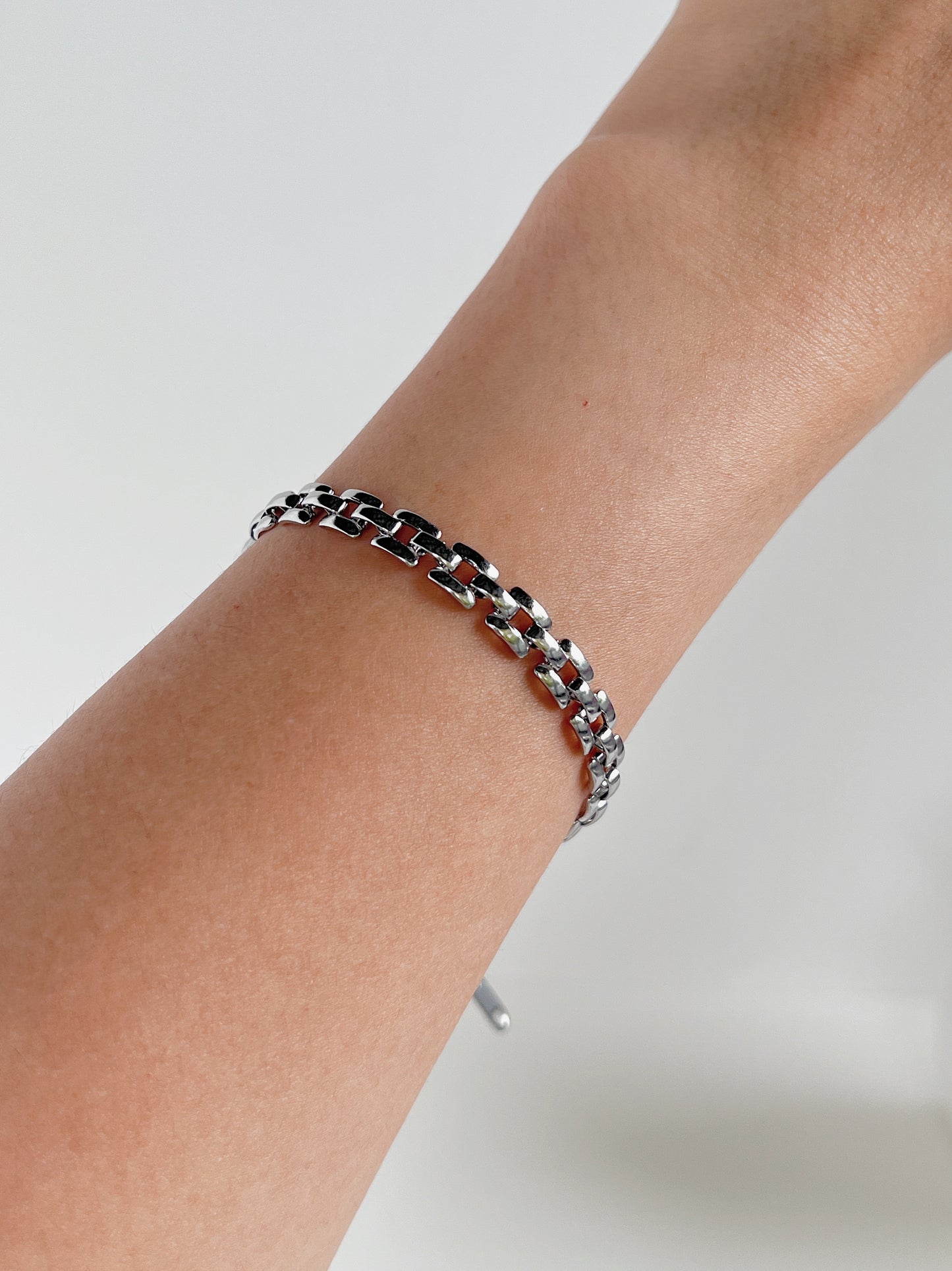 Studio hand shot of a model with the polished Evie silver link bracelet catching bright natural sunlight on her wrist.