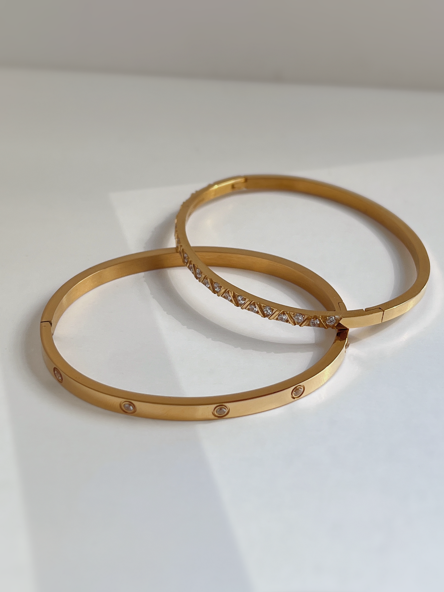 The Dane and Gia gemstone bangles in polished gold, illustrating the sleek, warm-toned modern luxury aesthetic.