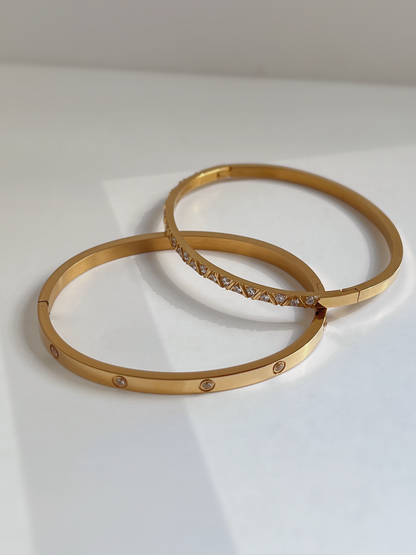 The Dane and Gia gemstone bangles in polished gold, illustrating the sleek, warm-toned modern luxury aesthetic.