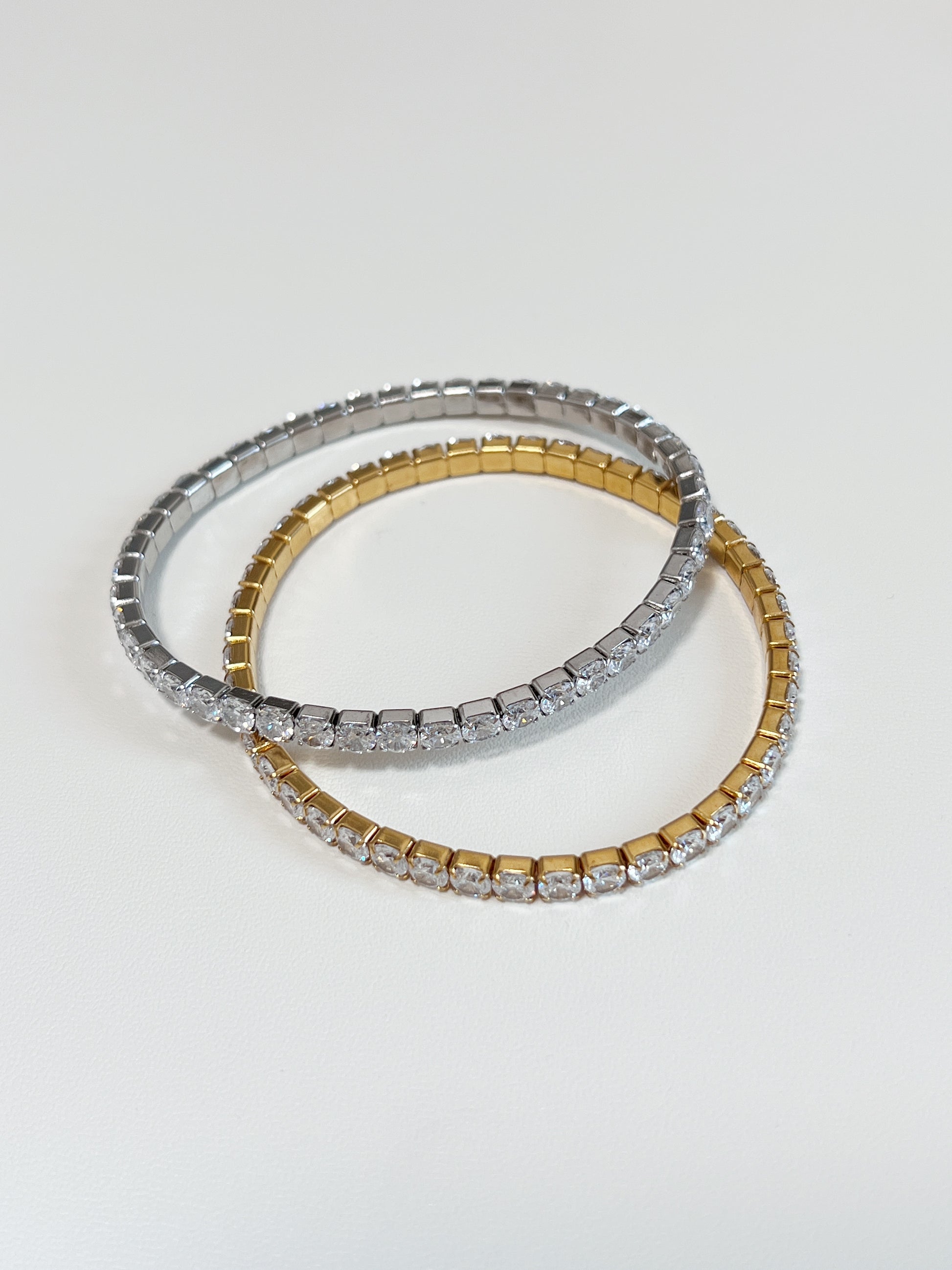 Overlapping gold and silver 4mm elastic tennis bracelets showcasing the smooth clasp-free stretch setting architecture.