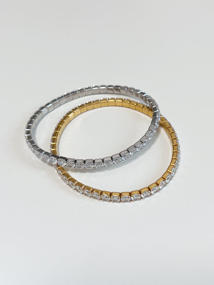Overlapping gold and silver 4mm elastic tennis bracelets showcasing the smooth clasp-free stretch setting architecture.
