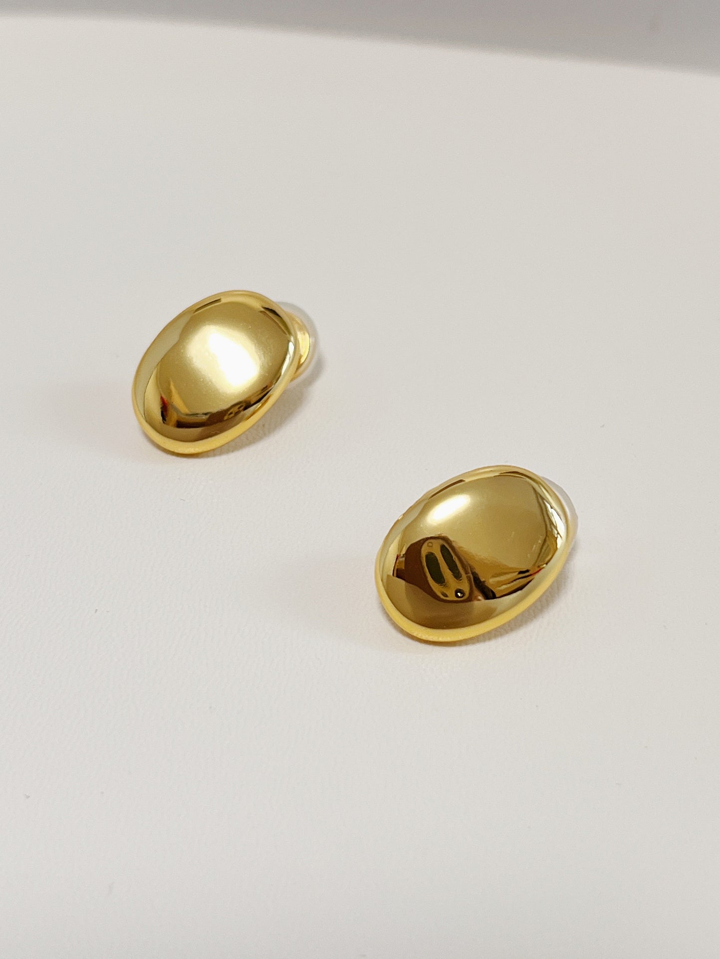 Symmetrical view of luxury plain gold oval clip earrings highlighting the brilliant light reflection on the convex surface.