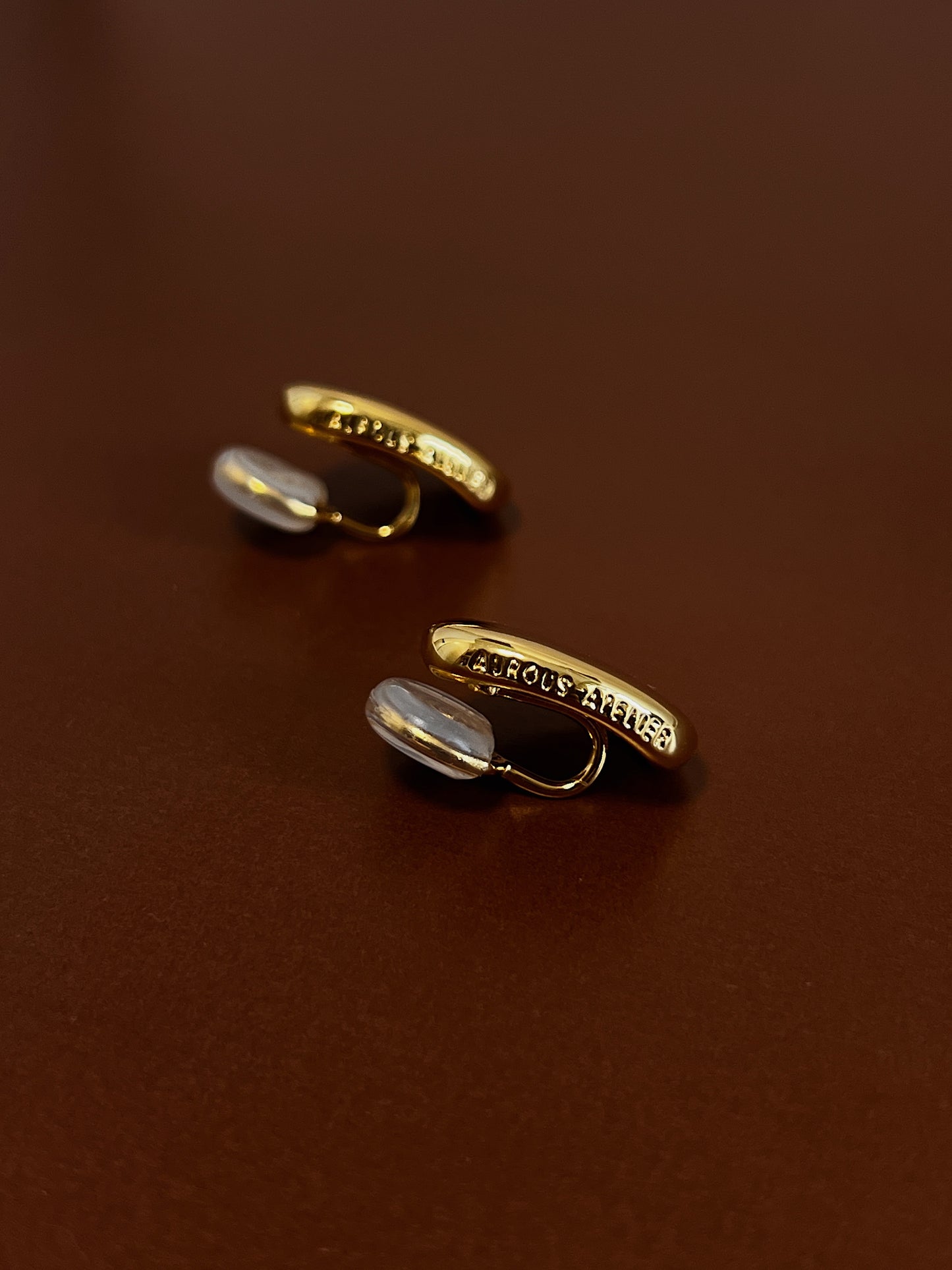 Macro product shot showing the signature brand name engraved on the side profile of the gold variant clip on earrings.