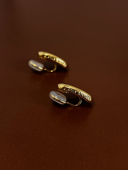 Macro product shot showing the signature brand name engraved on the side profile of the gold variant clip on earrings.