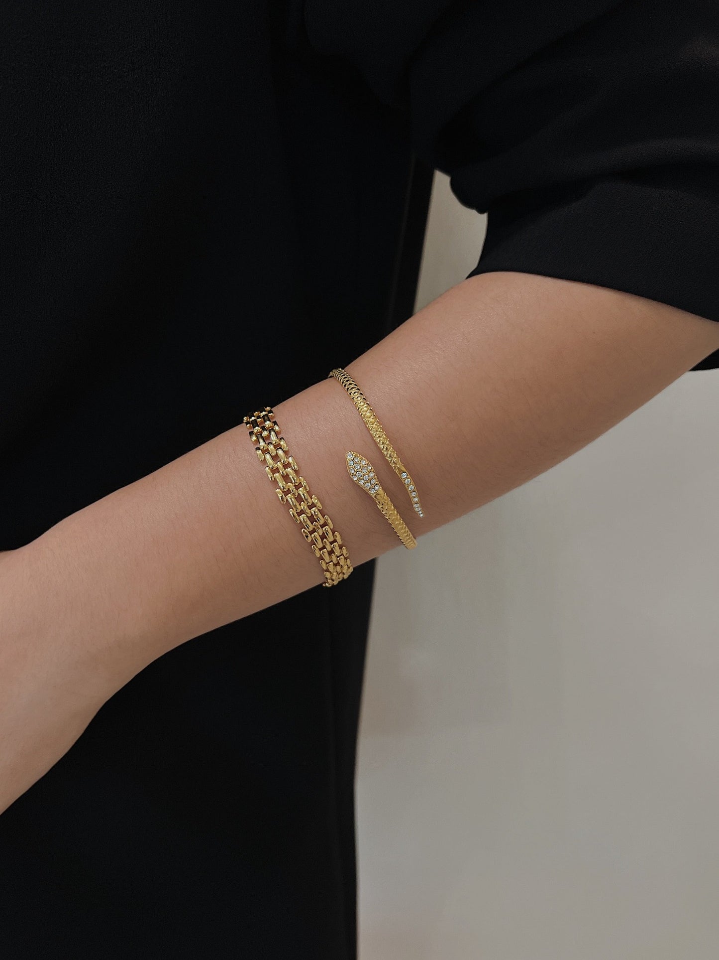 Model wrist wearing the gold Isa Serpent Bangle stacked with a mesh link bracelet paired with a black tailored blazer.
