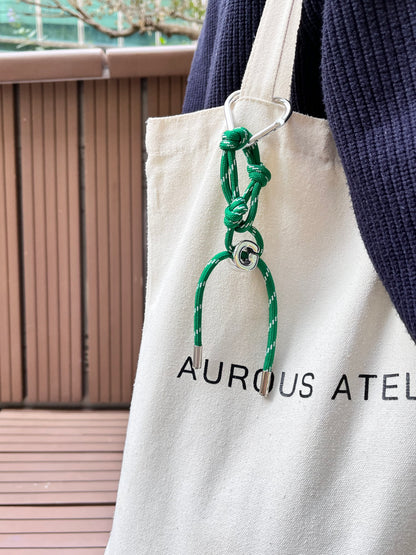 Close up style lookbook capture highlighting a custom initial loop ornament hanging from aurous atelier canvas tote bag