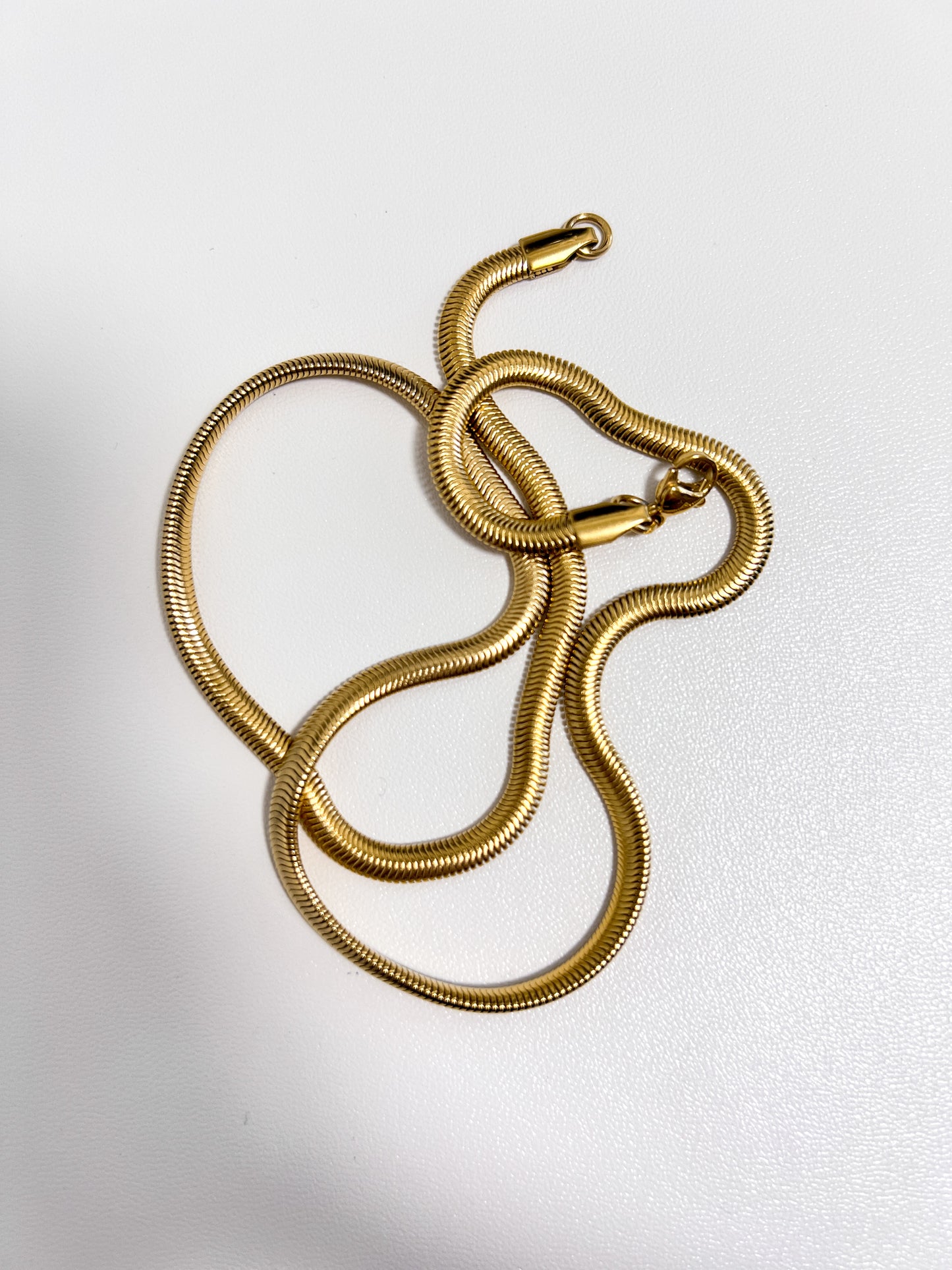 Aurous Atelier minimalist product display illustrating the supple fluid drape of a flat steel core chain