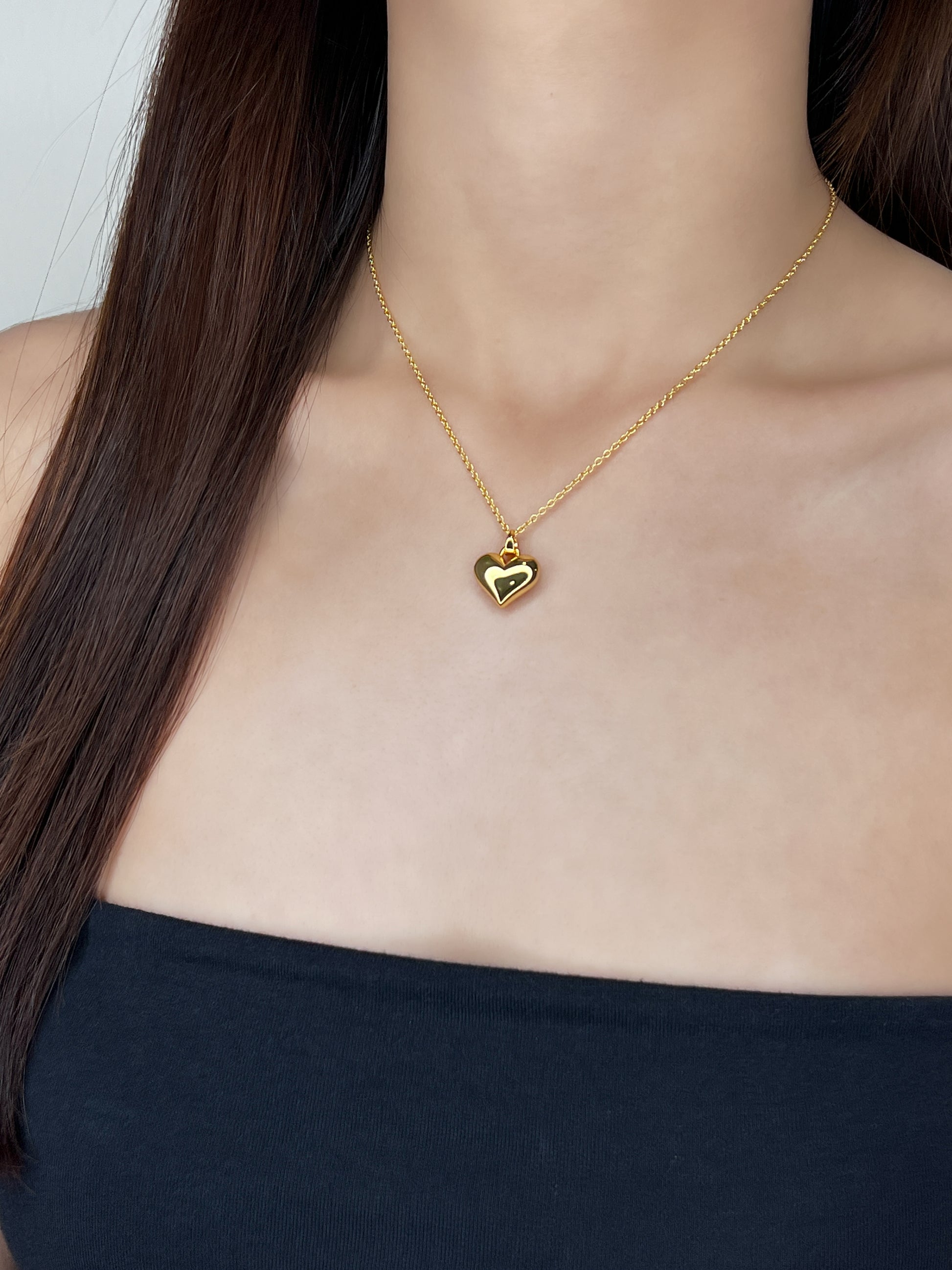 Front lookbook framing of a model wearing a high-shine solid 3D heart pendant sitting clean against a bare collarbone and a minimal tube top