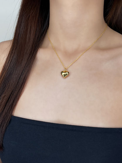 Front lookbook framing of a model wearing a high-shine solid 3D heart pendant sitting clean against a bare collarbone and a minimal tube top