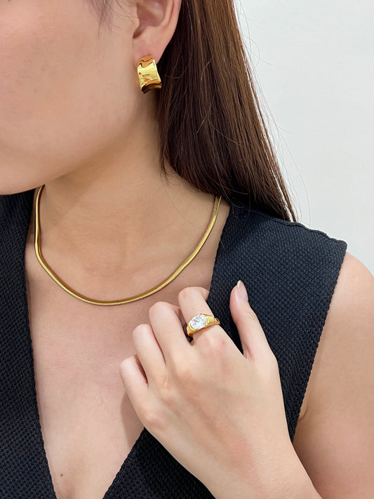 Front lookbook perspective of a wide flat gold herringbone chain lying beautifully across a bare collarbone