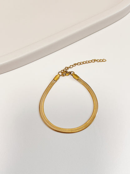 Overhead product view of the Bec gold snake chain bracelet resting in a clean loop on a minimalist white display surface, highlighting the secure lobster clasp and adjustable extension chain