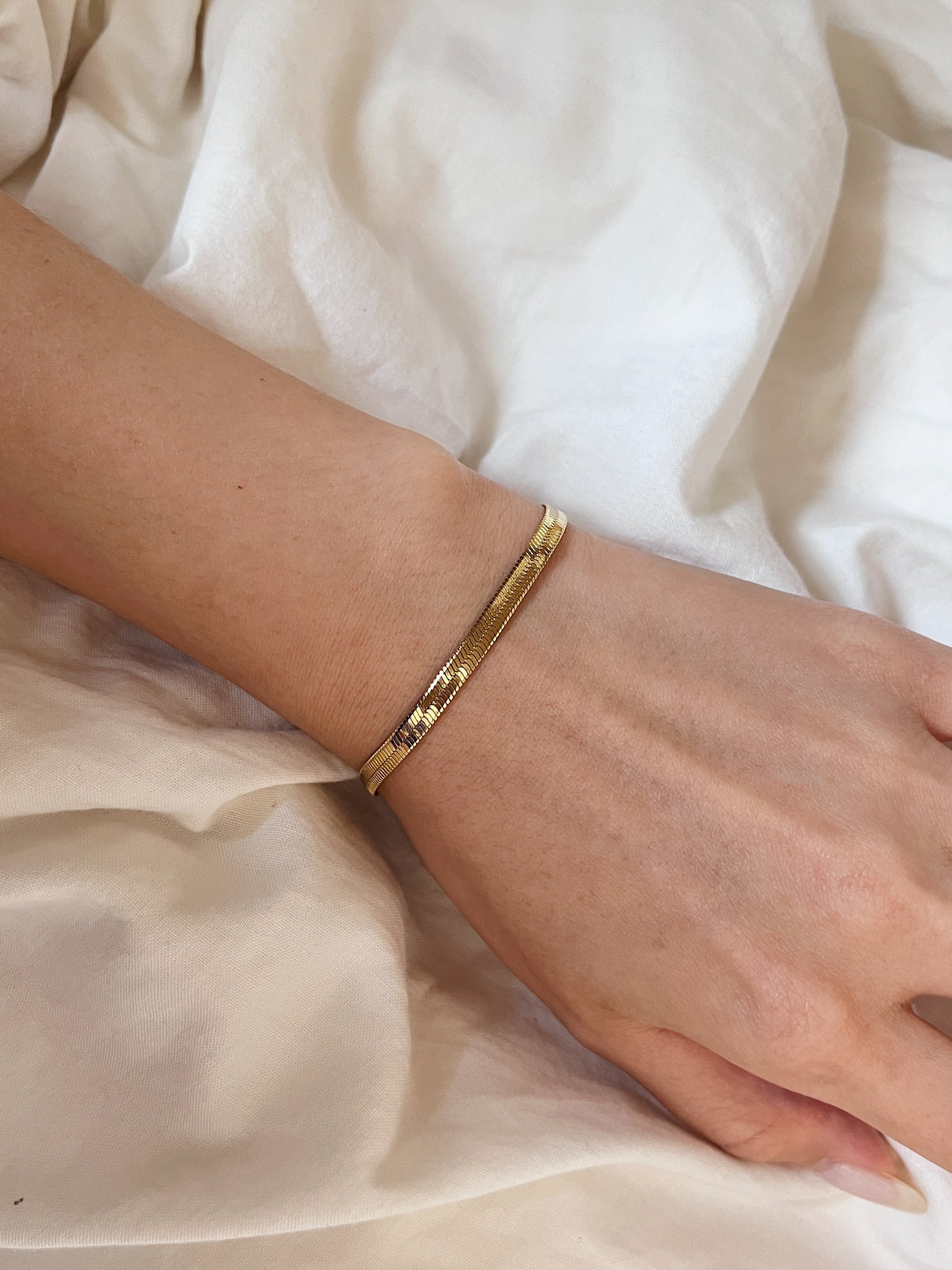Top-down shot showcasing the fluid drape of the golden serpentine bracelet against a soft cream background