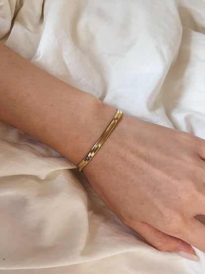 Top-down shot showcasing the fluid drape of the golden serpentine bracelet against a soft cream background