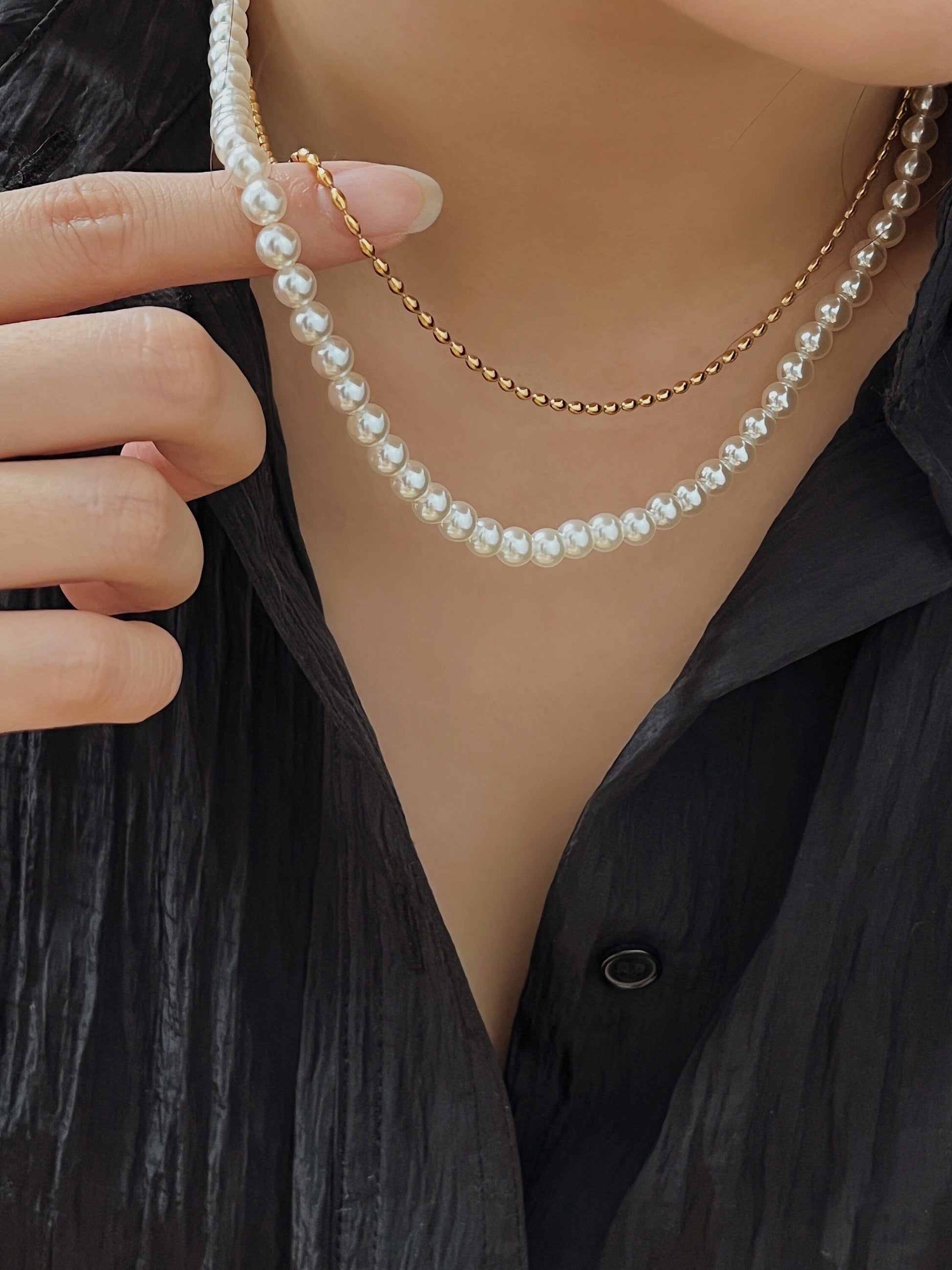 Front perspective of a delicate gold rice bead choker nesting on a collarbone with an open black shirt