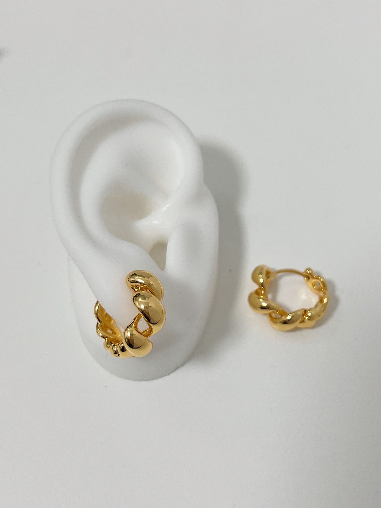 Gold Twisted Earrings showcasing on a fake ears