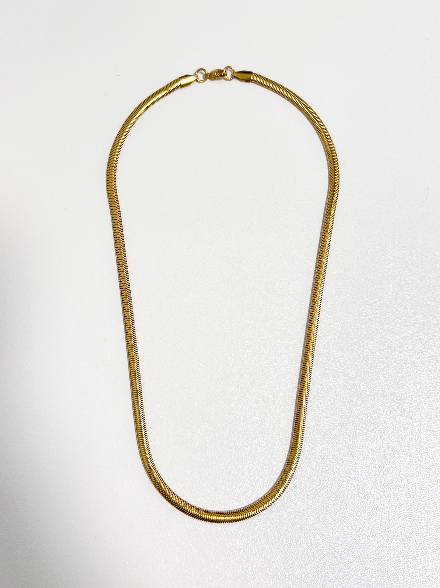 Studio view of the Bryony snake chain necklace showing its flat 5mm gold liquid metal profile on a white surface