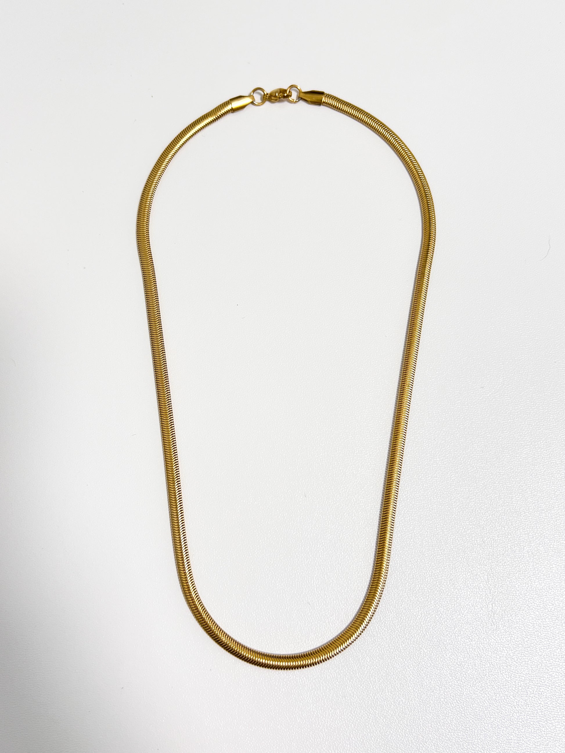 Studio view of the Bryony snake chain necklace showing its flat 5mm gold liquid metal profile on a white surface