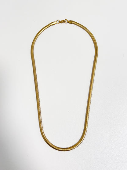 Studio view of the Bryony snake chain necklace showing its flat 5mm gold liquid metal profile on a white surface