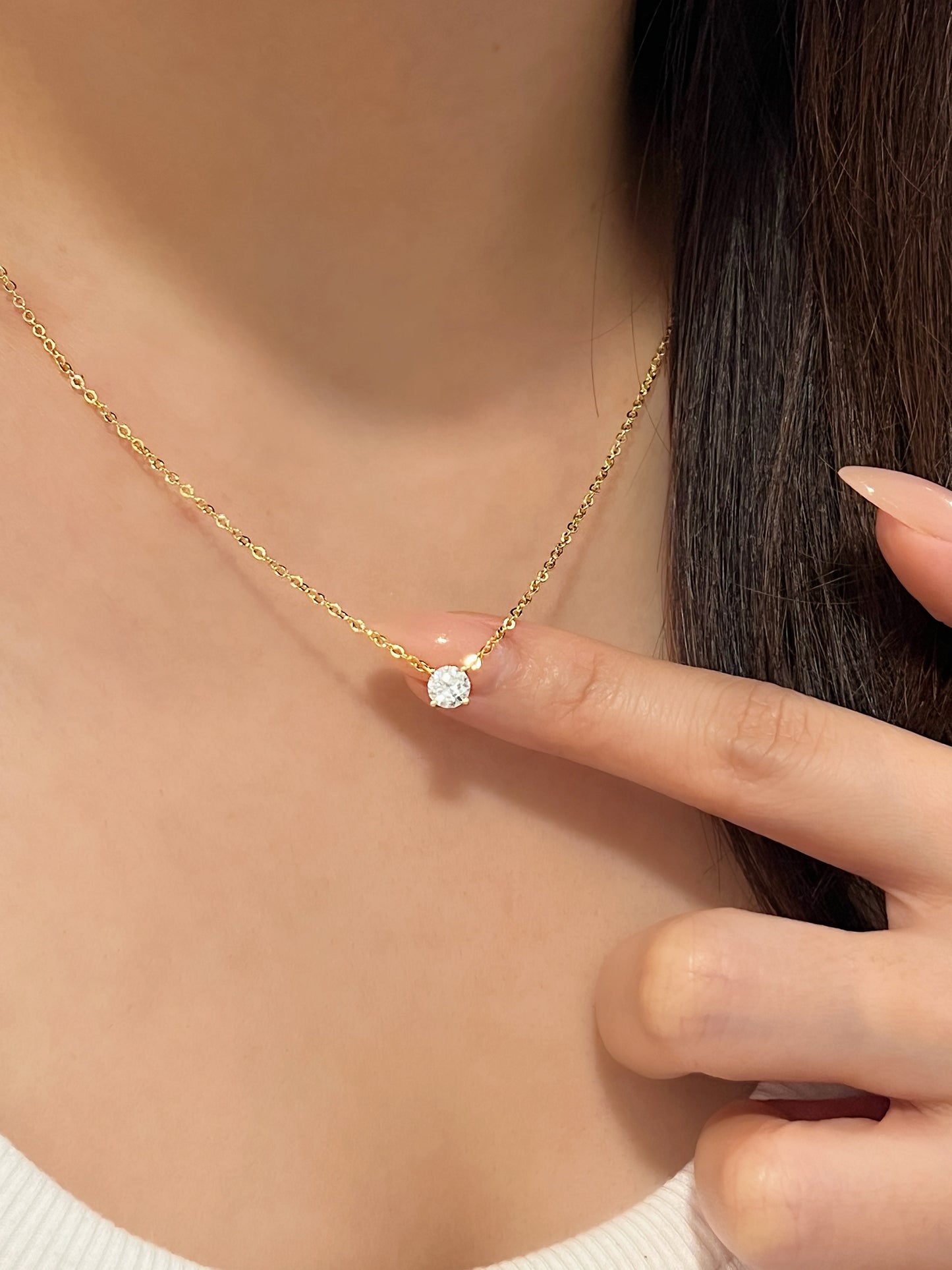 Model finger pointing directly to 14k gold plated Cala round VVS1 moissanite solitaire pendant resting on collarbone