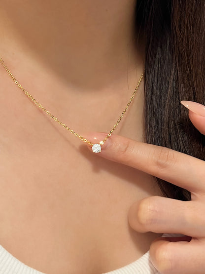 Model finger pointing directly to 14k gold plated Cala round VVS1 moissanite solitaire pendant resting on collarbone