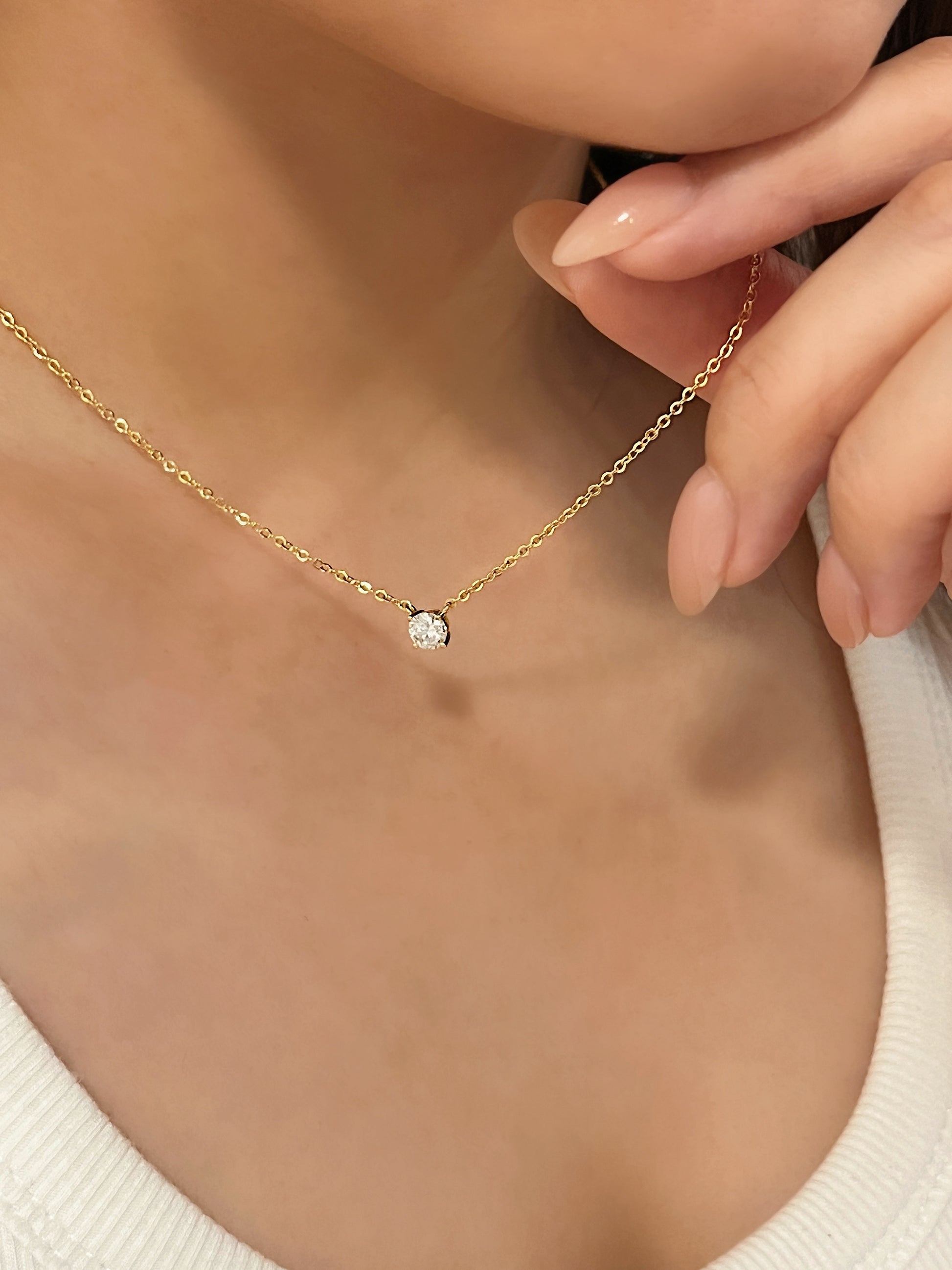 Model holding fine trace chain of 14k gold plated Cala moissanite solitaire pendant necklace worn with white ribbed top