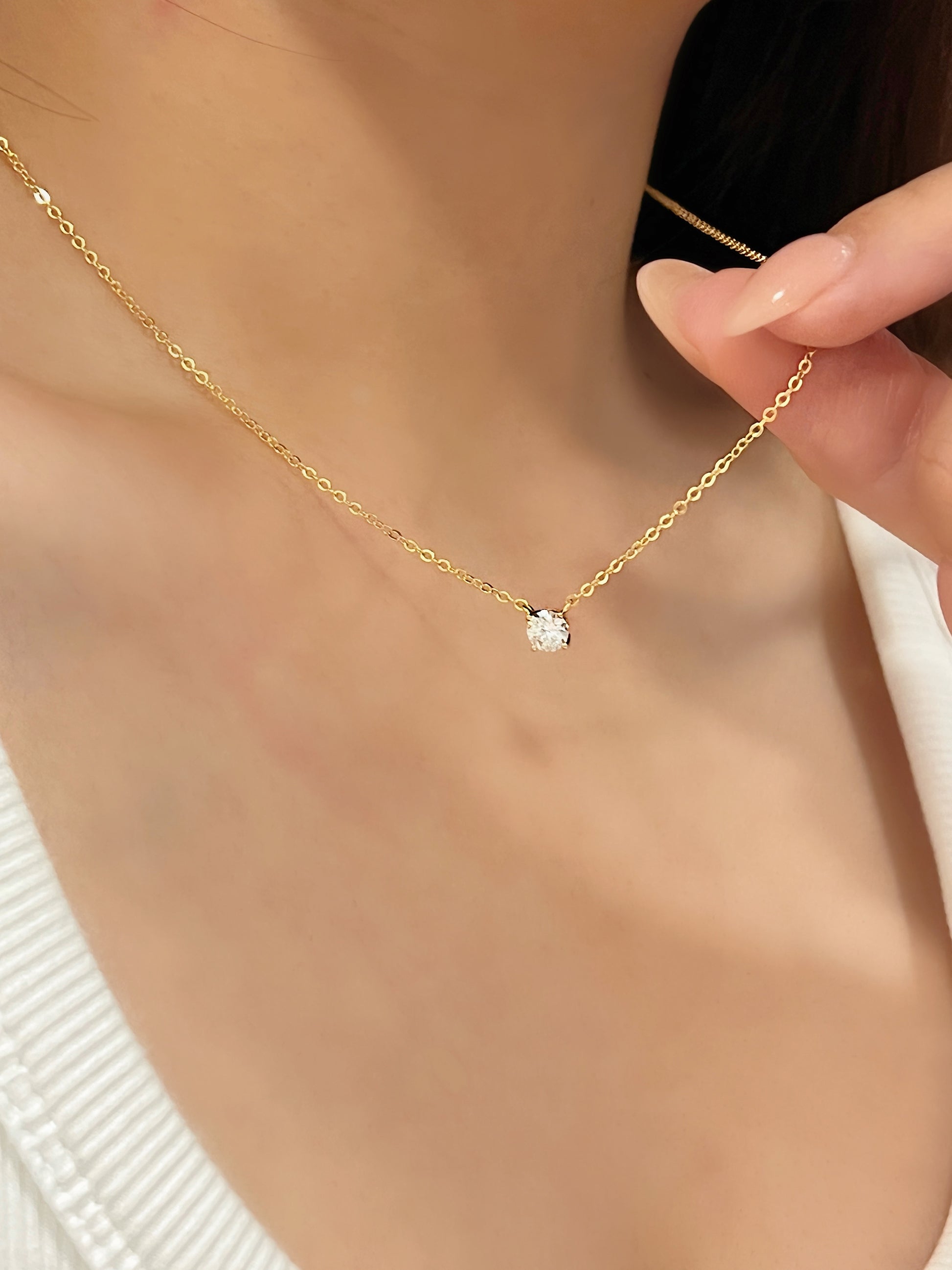 Model fingers holding fine trace chain of Cala 14k gold plated moissanite solitaire pendant necklace on collarbone