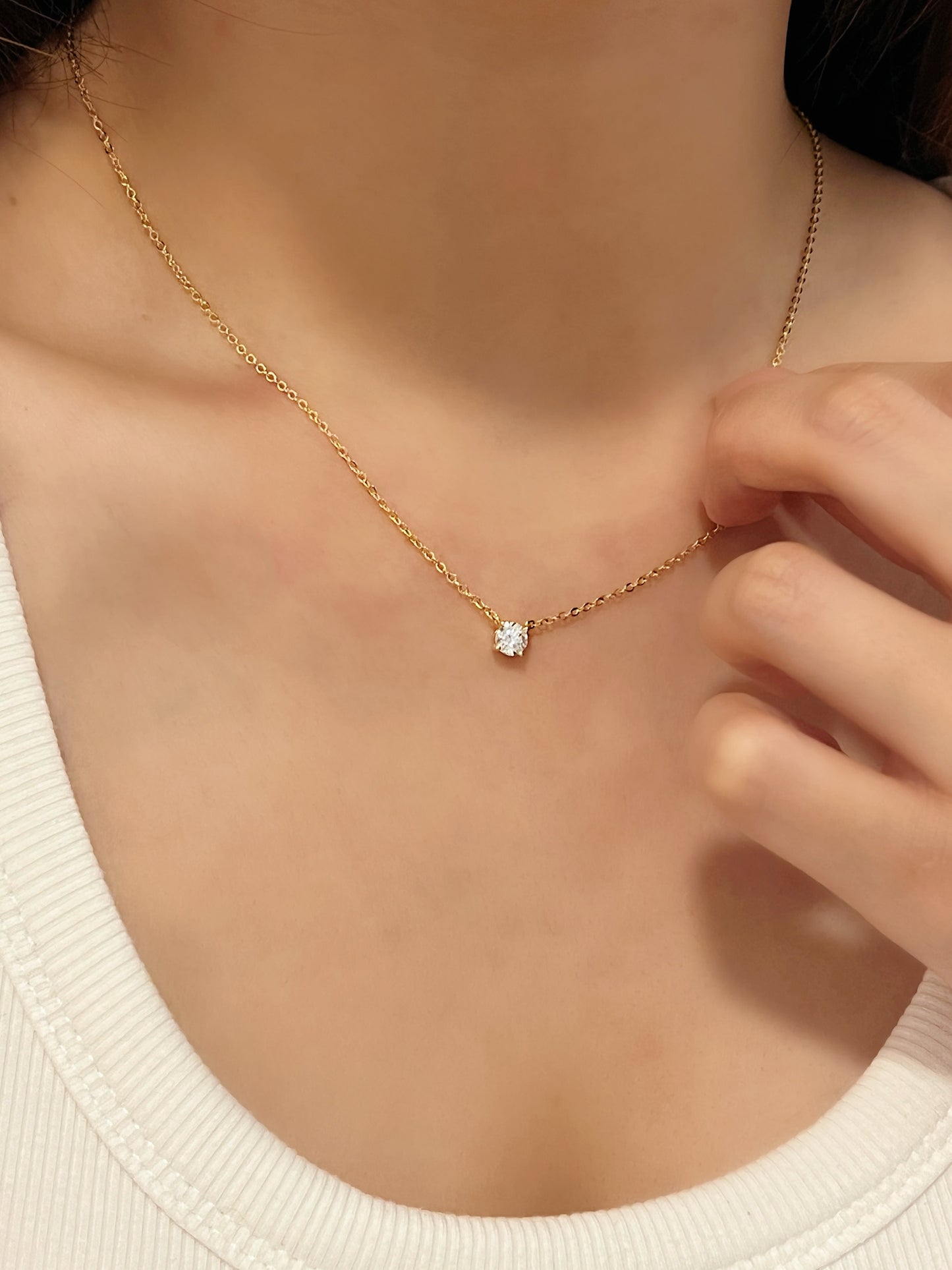 Close up view of model hand touching 14k gold finish Cala VVS1 moissanite solitaire necklace resting on collarbone