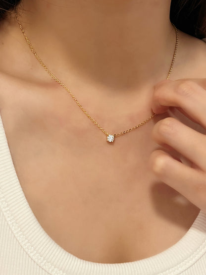 Close up view of model hand touching 14k gold finish Cala VVS1 moissanite solitaire necklace resting on collarbone
