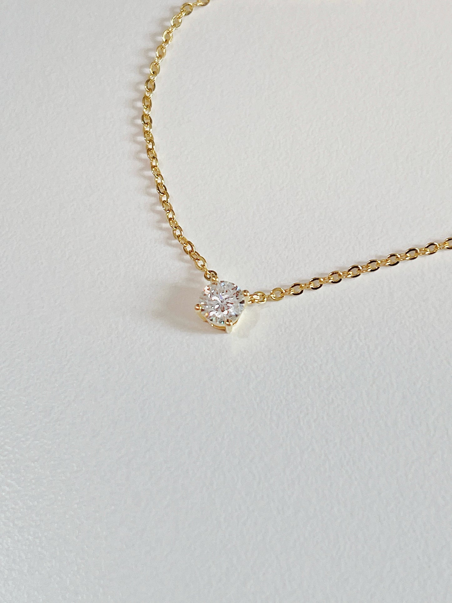 Macro view of 4-prong basket setting elevating VVS1 round moissanite stone on Cala brass necklace