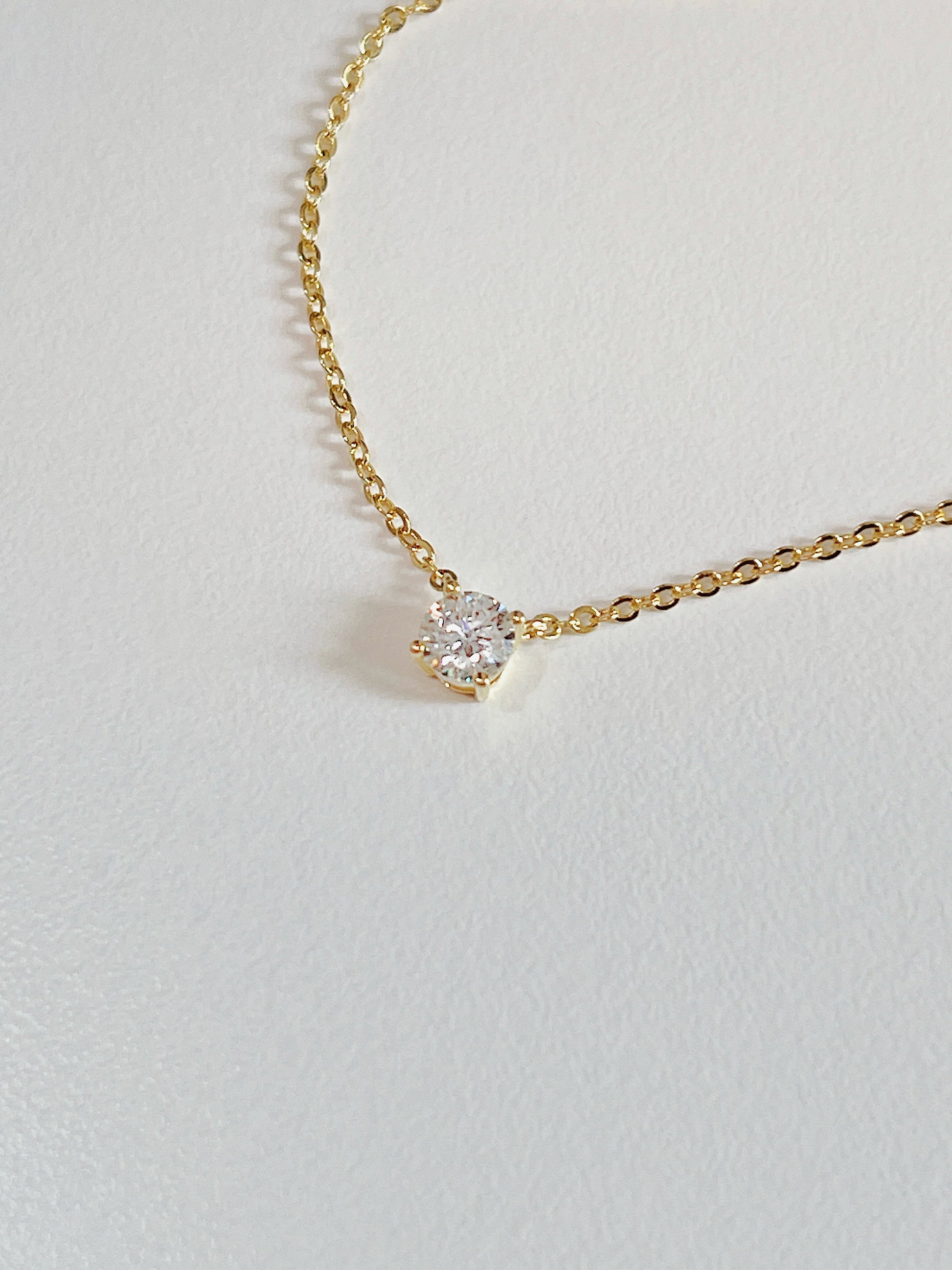 Macro view of 4-prong basket setting elevating VVS1 round moissanite stone on Cala brass necklace