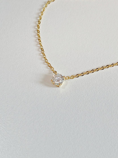 Macro view of 4-prong basket setting elevating VVS1 round moissanite stone on Cala brass necklace