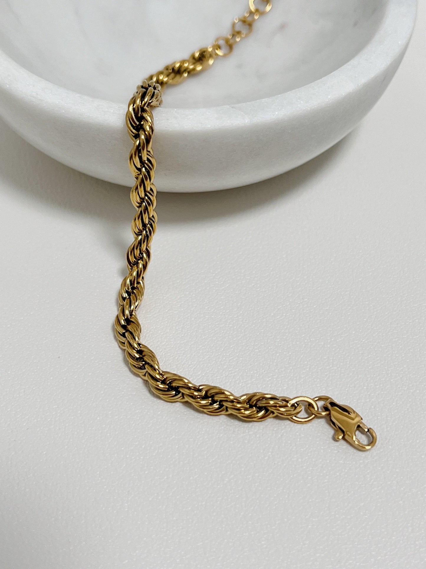 A top-down shot of the Cali 5mm gold twisted rope bracelet draped over the edge of a white porcelain bowl.