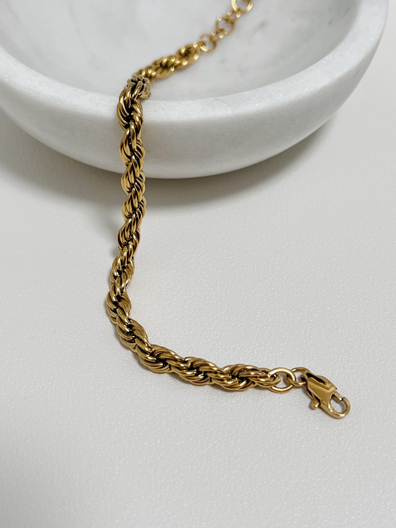 A top-down shot of the Cali 5mm gold twisted rope bracelet draped over the edge of a white porcelain bowl.
