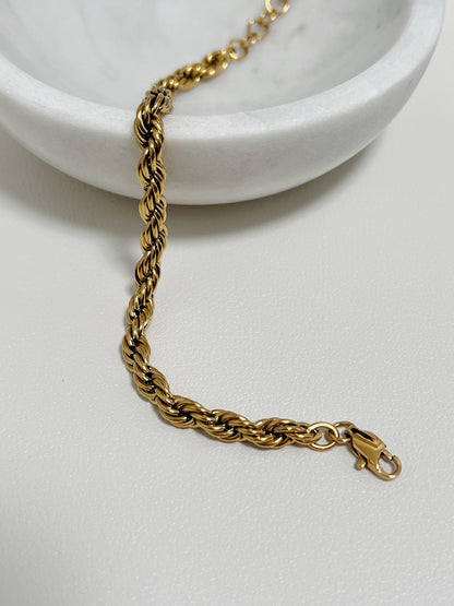 A top-down shot of the Cali 5mm gold twisted rope bracelet draped over the edge of a white porcelain bowl.