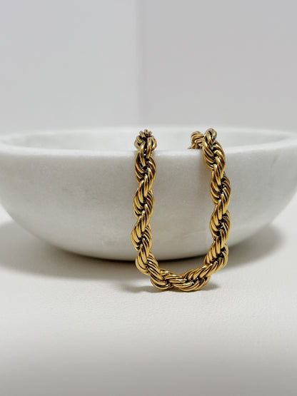 The Cali 18K gold PVD twisted rope bracelet coiled neatly inside a luxury white ceramic jewelry dish.