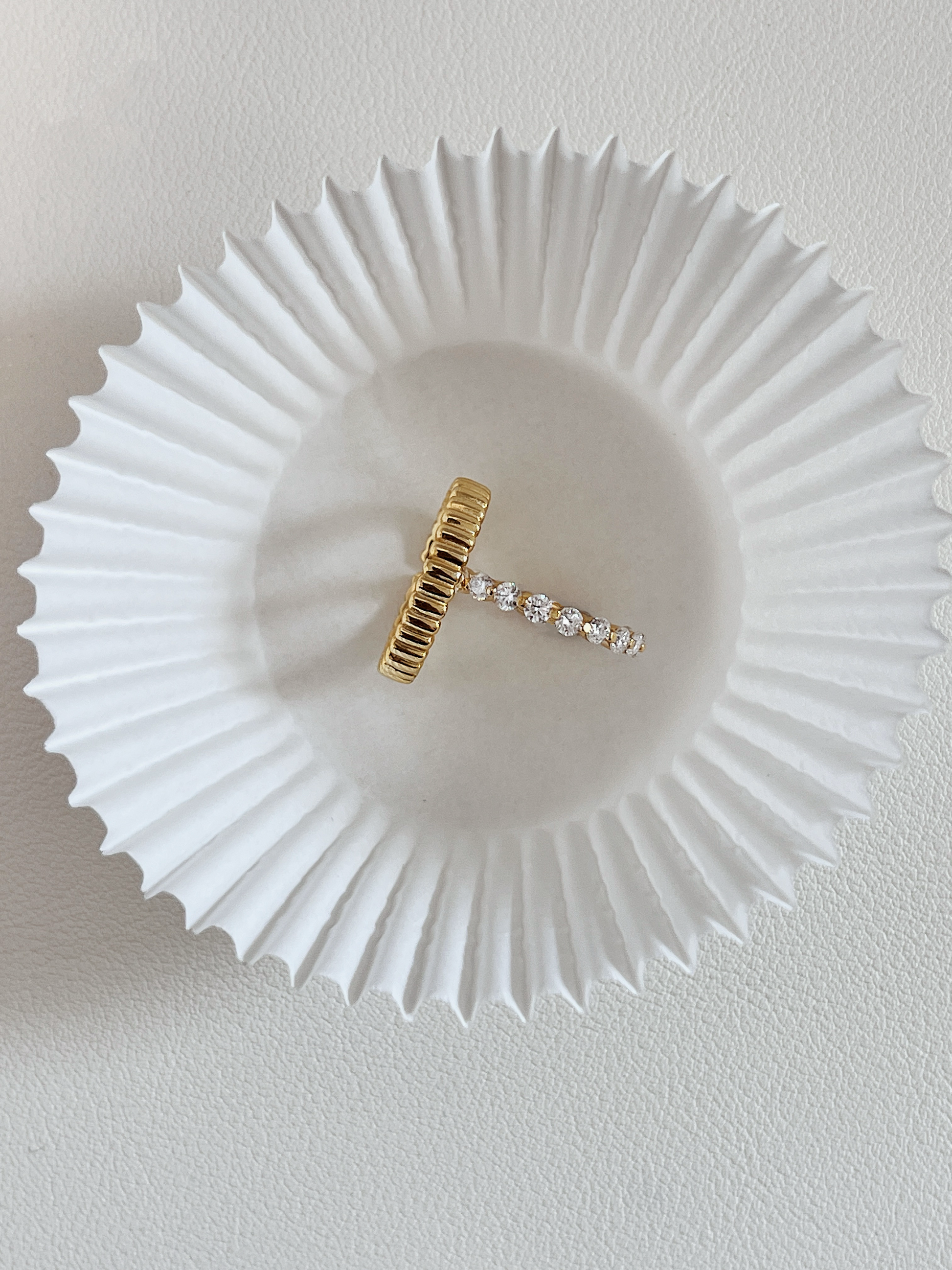 Overhead studio shot of the Callie moissanite eternity ring balanced perpendicularly inside a slim vede gold ribbed dome band on a white baking paper cup